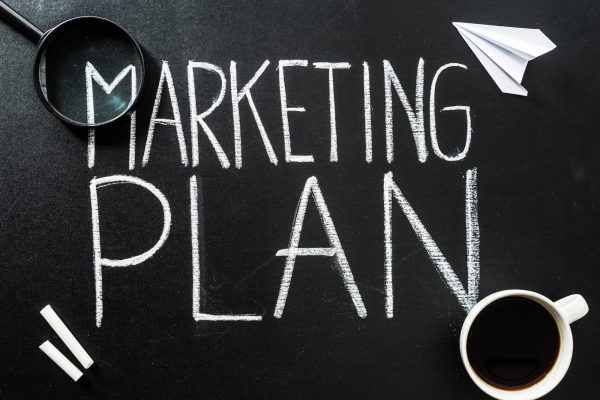 Top view of marketing plan lettering on chalkboard with cup of coffee and magnifier
