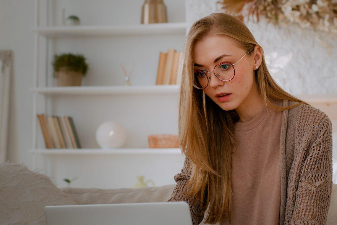 Caucasian shocked woman in glasses looking at laptop reading bad news close mouth with hands holding