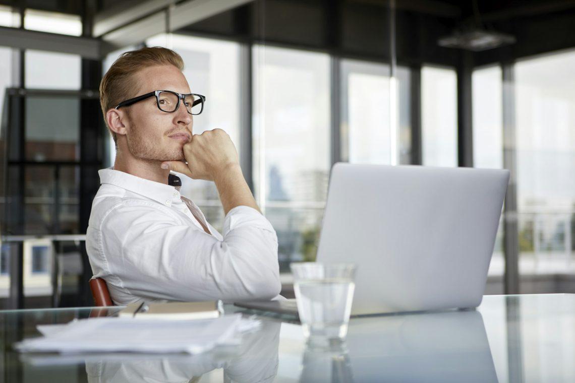 Businessman with laptop on desk in office thinking