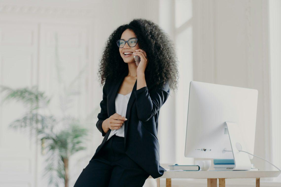 Happy female entrepreneur shares ideas for project with colleague, holds modern cell phone