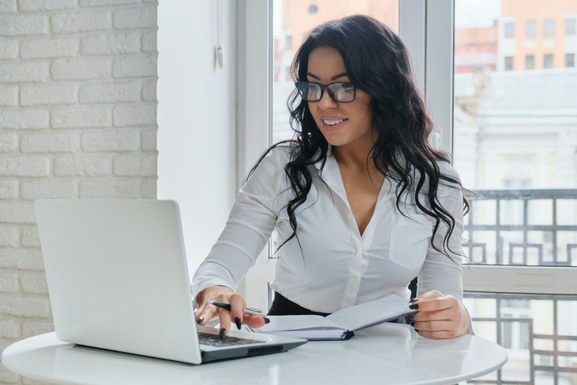 Beautiful business woman working with laptop, sitting at desk near window